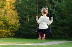A little girl swinging in front of a pathway into a forest.